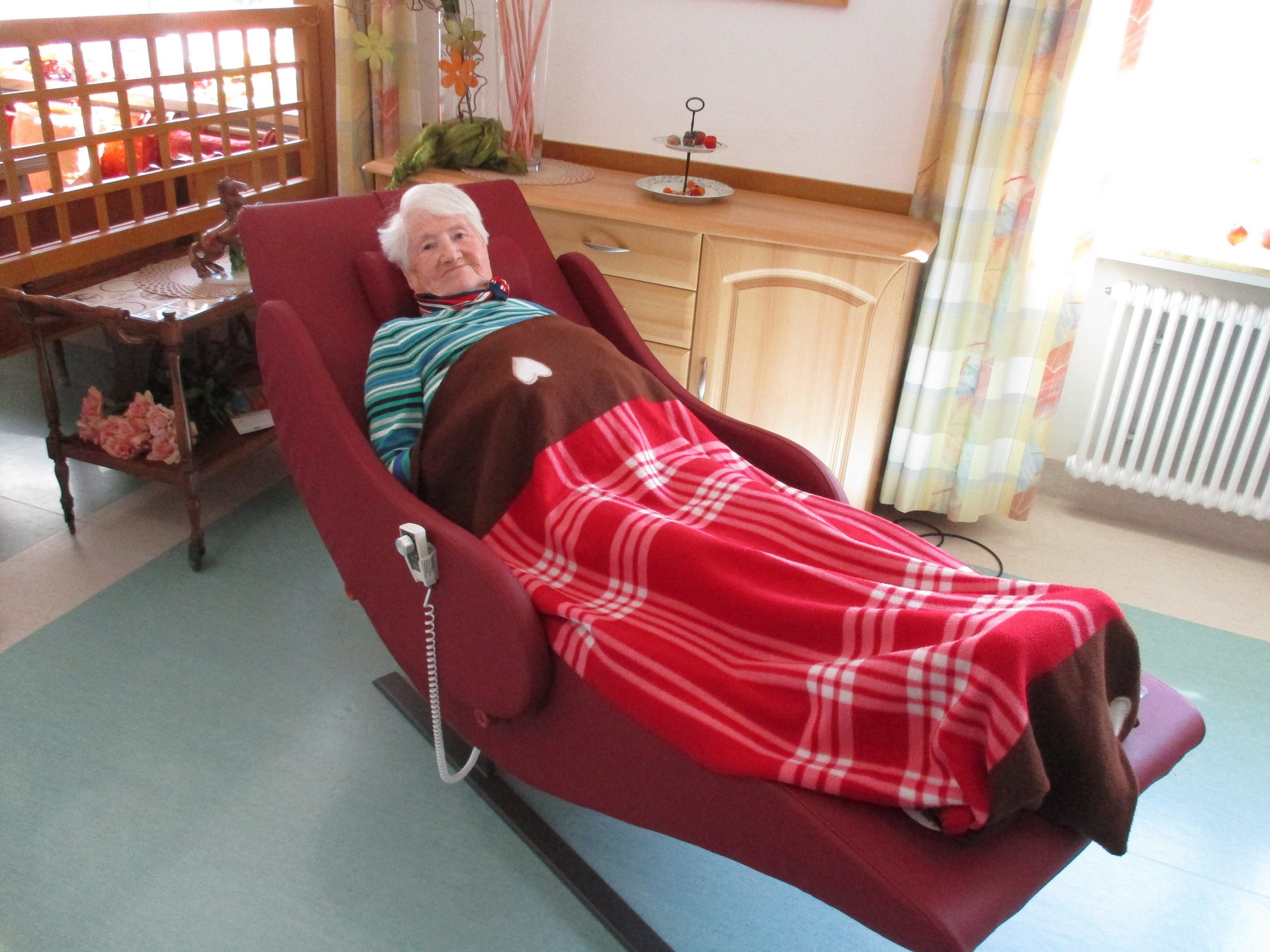 Eine Seniorin liegt - in eine Decke gekuschelt - auf einer Liege. 