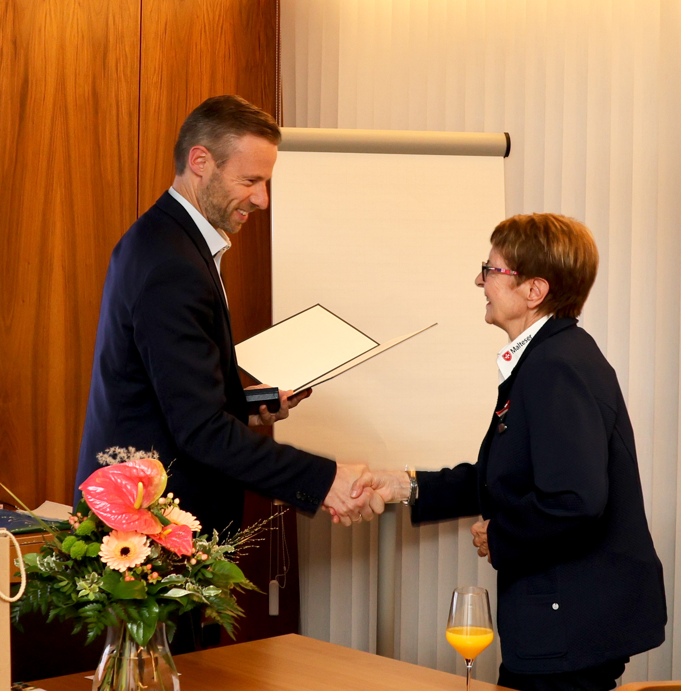 Landrat Alex Eder überreicht Silvia Schwarz eine Urkunde und reicht ihr die Hand. 