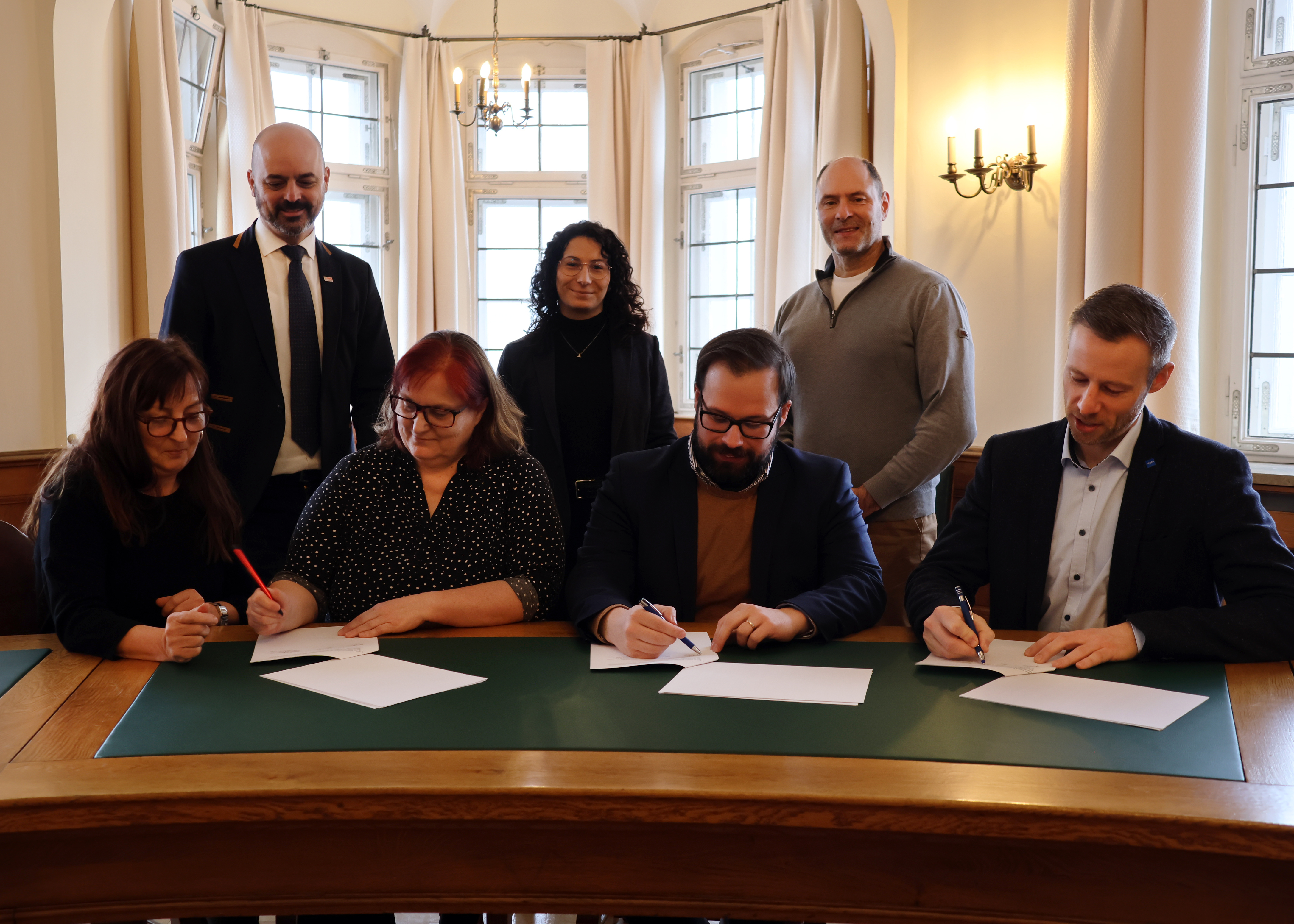 Vertreterinnen des Frauenhauses, der Oberbürgermeister der Stadt Memmingen Jan Rothenbacher und Landrat Alex Eder unterzeichnen den Vertrag. Dahinter stehen Vertreter der Stadt und des Landkreises. 