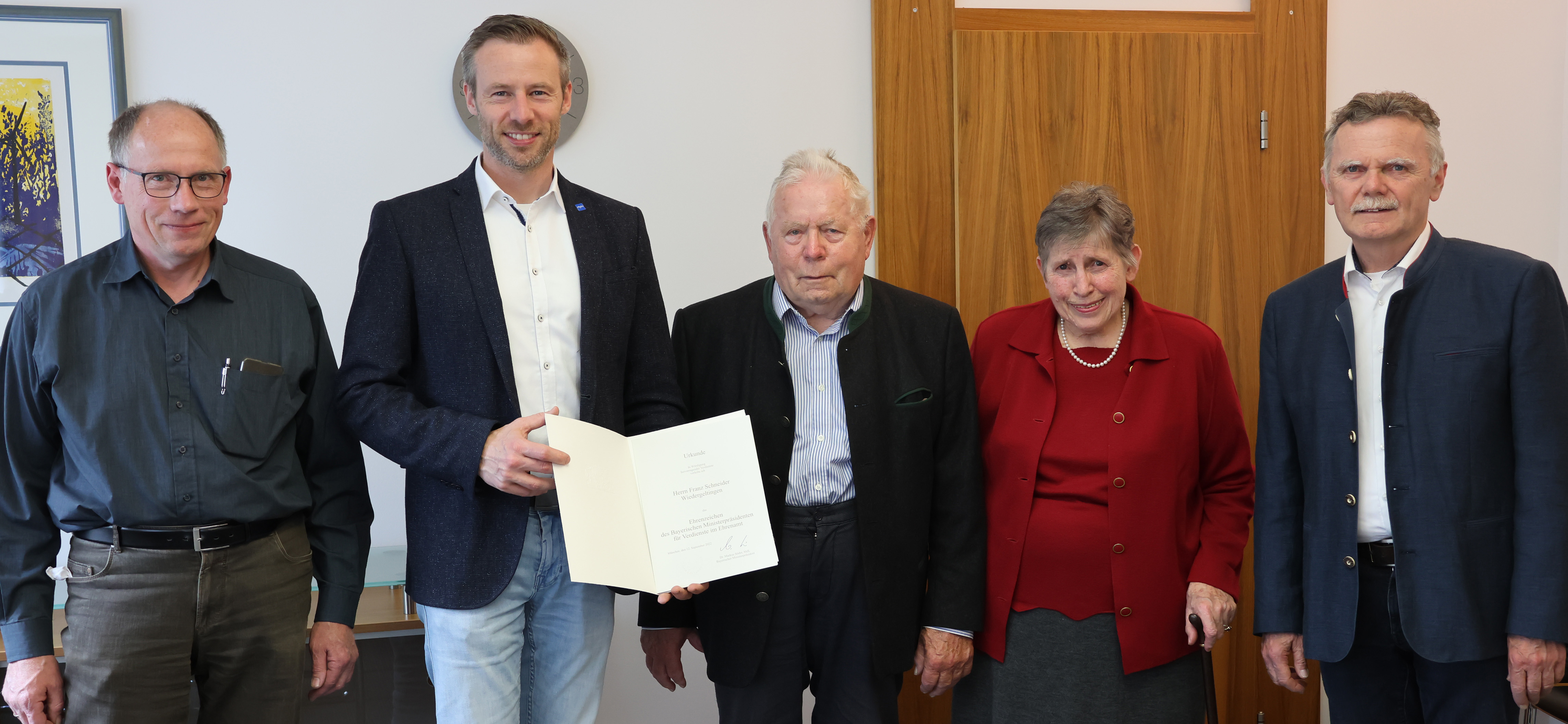 Landrat Alex Eder und der Geehrte Franz Schneider halten eine Urkunde in die Kamera, neben ihnen steht links der Sohn des Geehrten, rechts seine Frau und der Bürgermeister von Wiedergeltingen, Norbert Führer. 