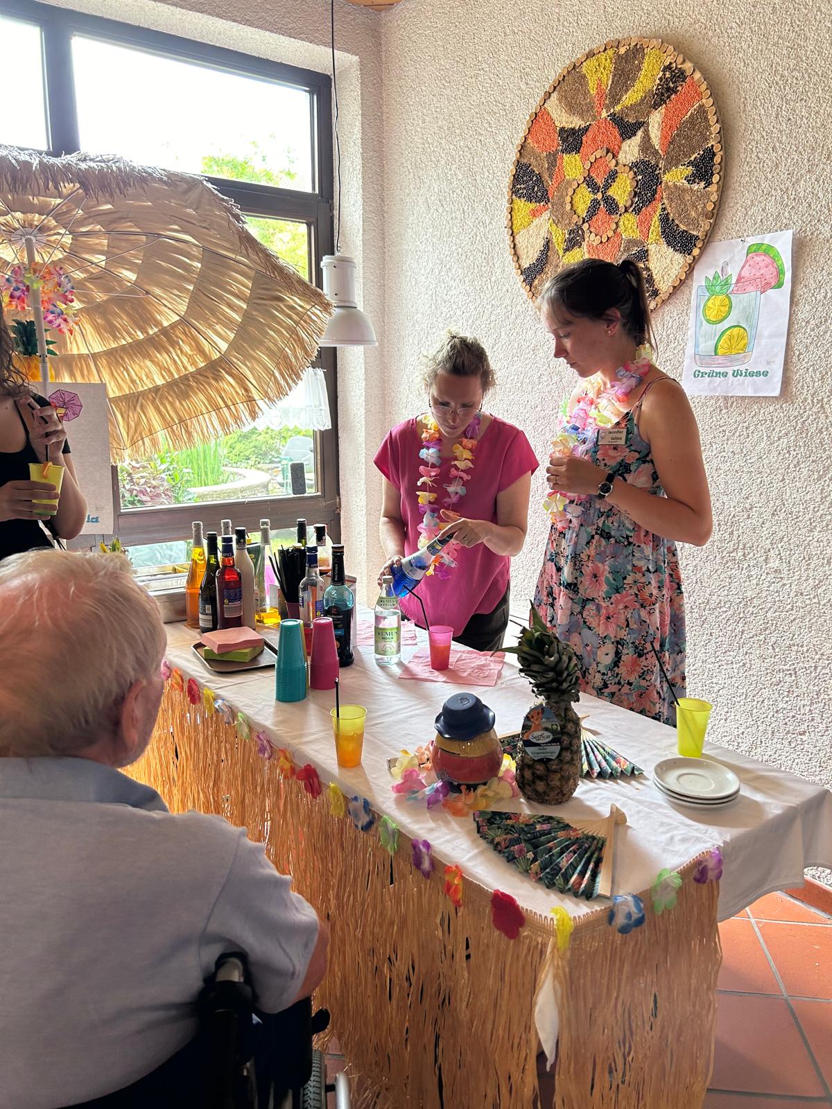 Zwei Damen mit Blumenketten um den Hals mischen Cocktails. 