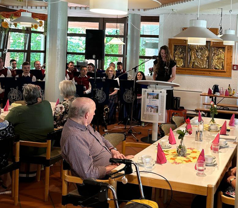 Im festlich geschmückten Saal sitzen Seniorinnen und Senioren an den Tischen. Im Hintergrund zu sehen: Der Orchesterverein Türkheim.