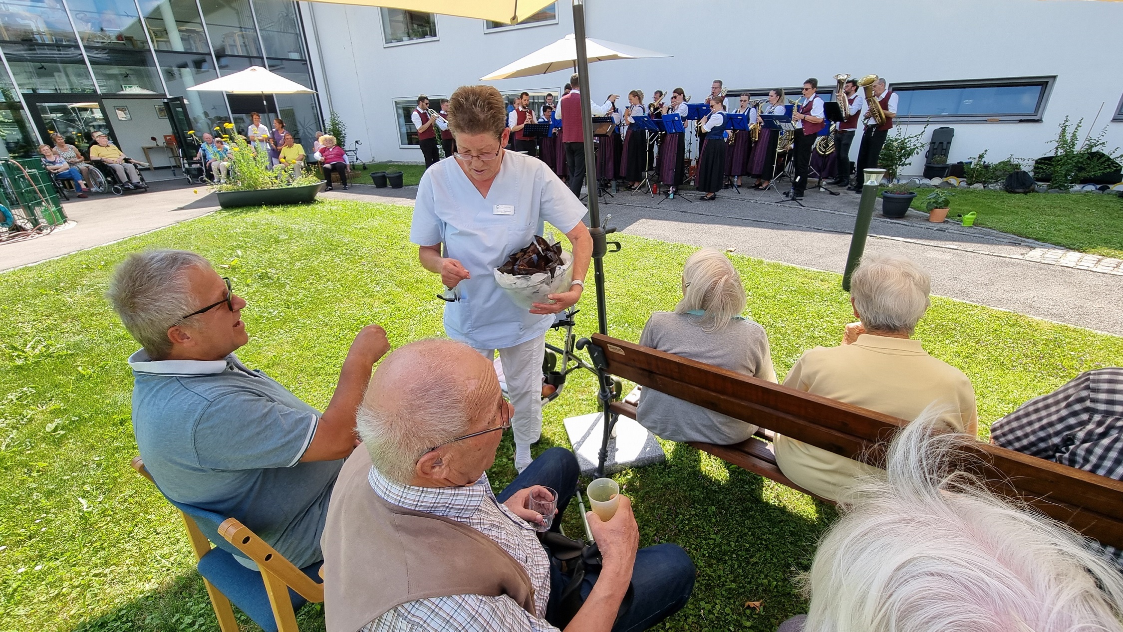 Eine Dame verteilt Eis an die Seniorinnen und Senioren. Im Hintergrund zu sehen: Die Stadtkapelle Bad Wörishofen. 